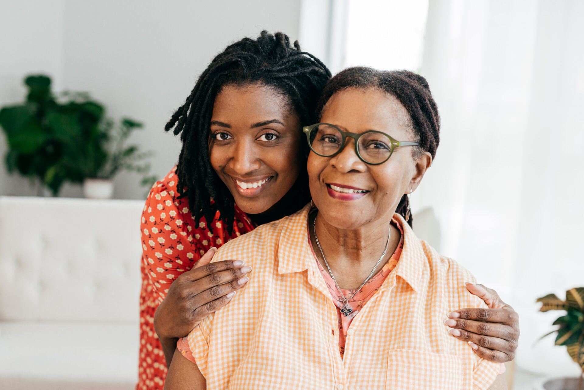 Portrait of a happy adult daughter with her hands on her mother's shoulders, smiling. Traditions at Solana.