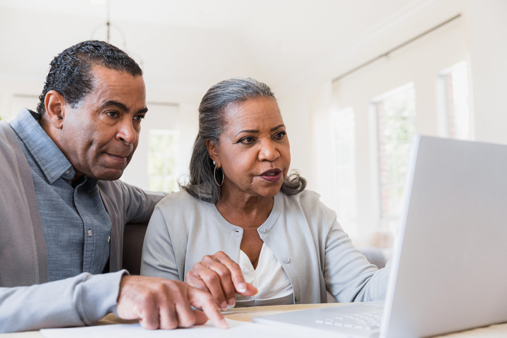 Senior man and woman sitting at their kitchen table looking at Traditions at Solana community information on a laptop