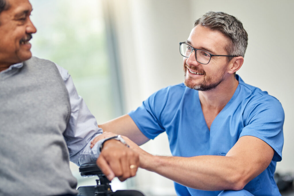 A male nurse sits next to an elderly resident and engage in a happy conversation and exchange smiles at Traditions of Solana.